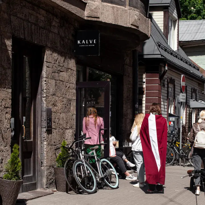 People standing outside a building with 'KALVE' sign, pedestrians and bicycles in the background