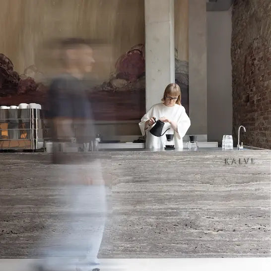 Person preparing coffee in a modern cafe setting with 'Kalve' branding.