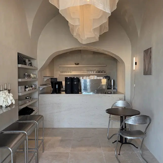 Modern coffee shop interior with counter, chairs, and shelves.
