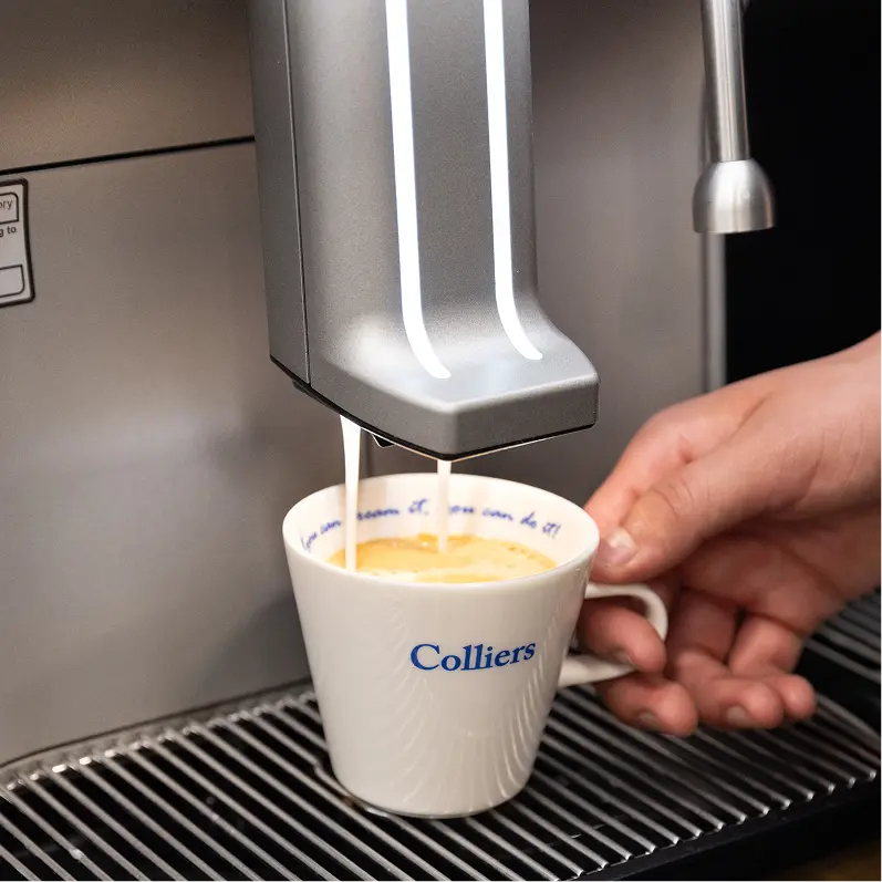Espresso being poured into a white cup with 'Colliers' branding, held by a hand.