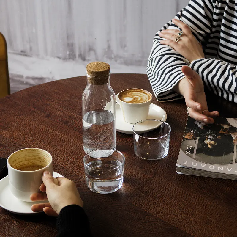 Two people sitting at a table with coffee cups, water glasses, and a book.