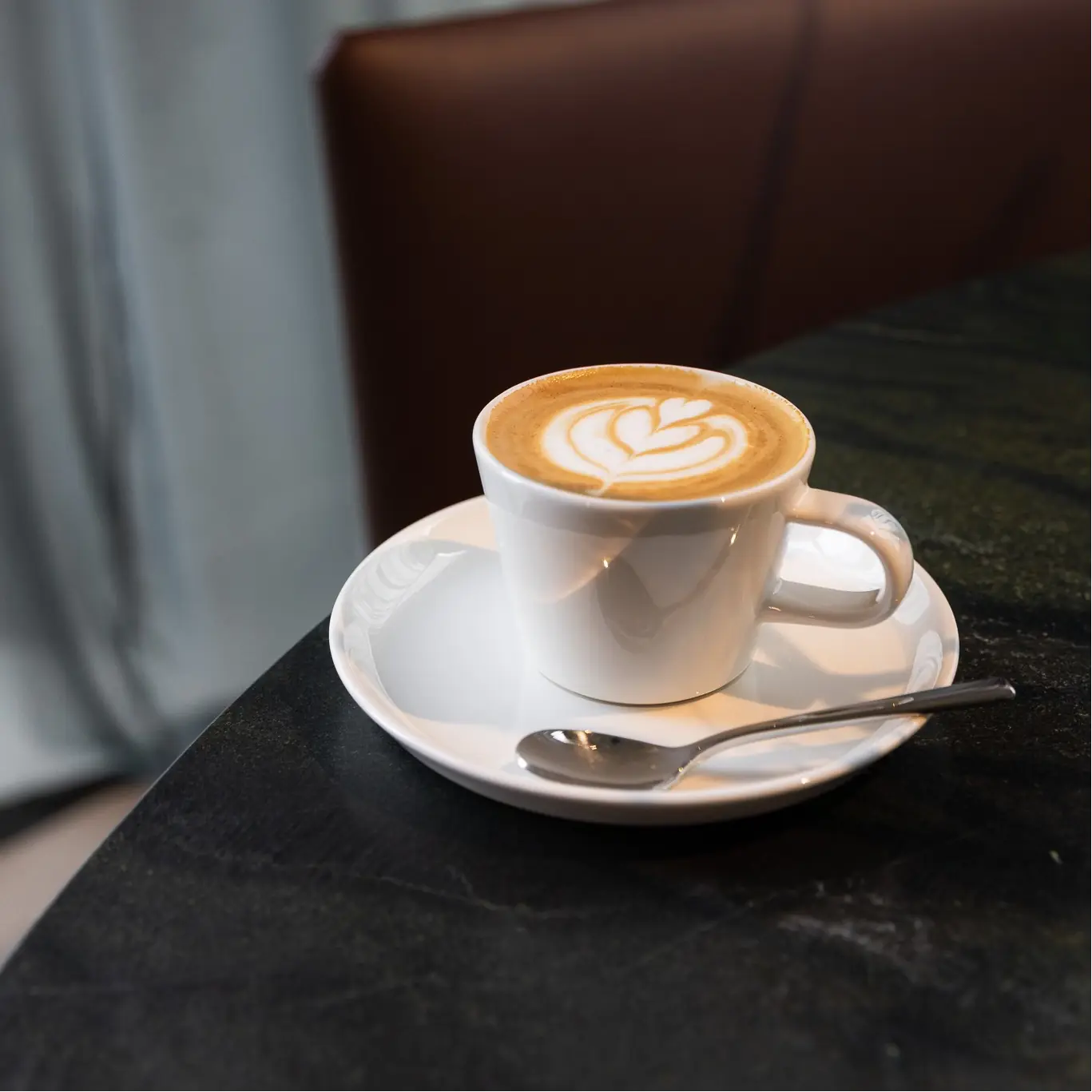 Cappuccino with latte art on a white cup and saucer on a dark surface.