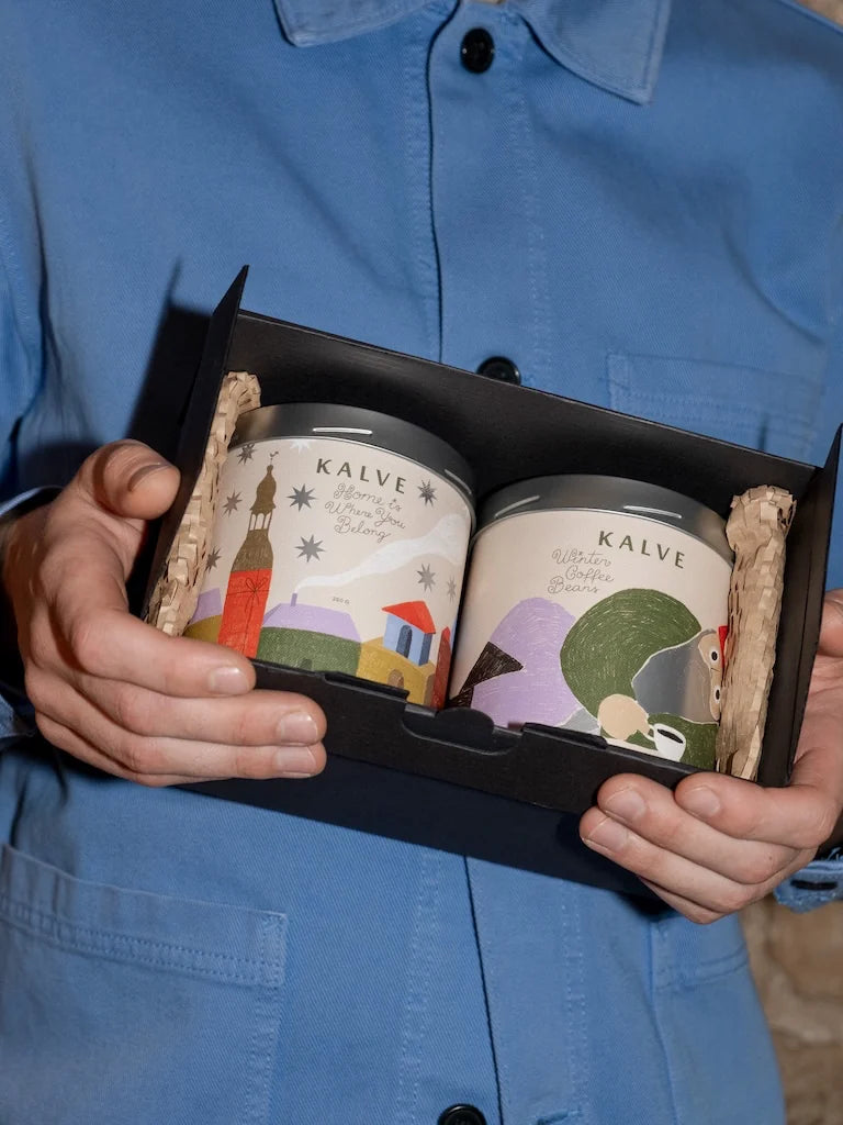 Two Kalve coffee tins  in a black box held by a person wearing a blue shirt.
