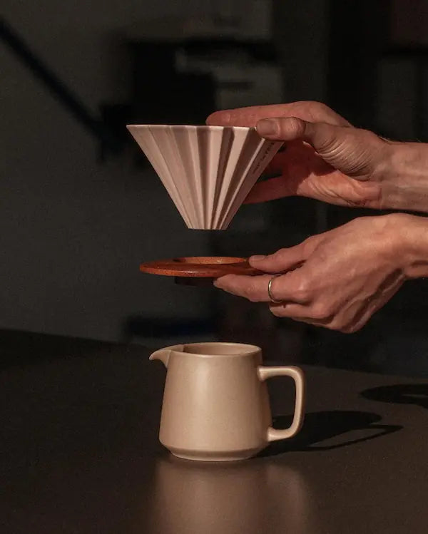 Person holding a wooden coffee filter over a ceramic pitcher on a dark surface